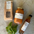Two bottles of tomato-based products and a small box on a concrete surface with a plant.